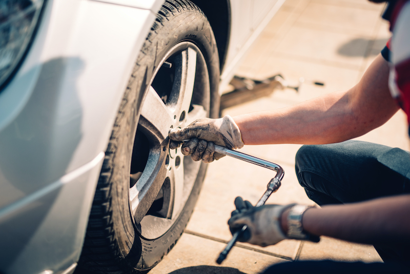 Tire maintenance, damaged car tyre or changing seasonal tires using wrench. Changing a flat car tire on the sideroad