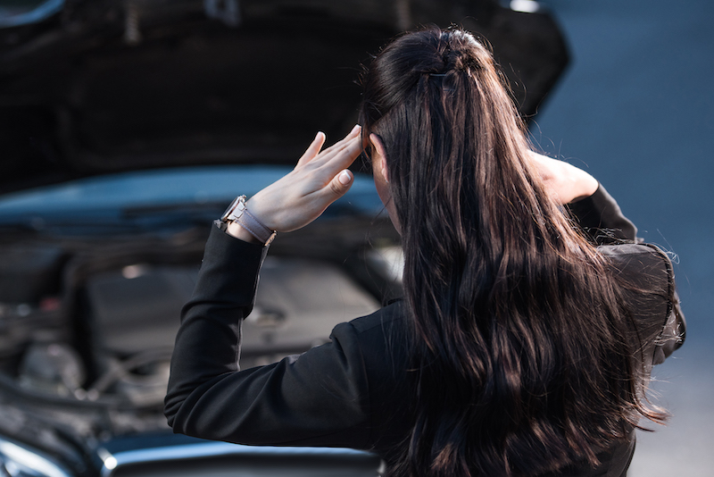 Car Transmission Problems, troubled woman looking at car engine.