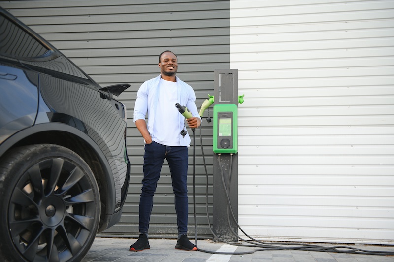 Car charging at home, man standing near home charging setup.