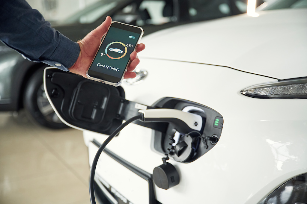Car charging at home, person monitoring EV charging using smart tech.