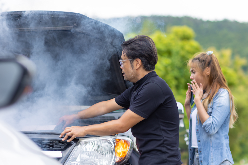 Car emergencies, man and woman watching smoking car engine.